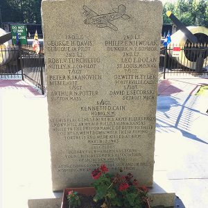 Stone monument with engraving of airplane in flight and text with names and flower bed at its base