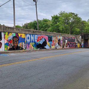 African-American figures and clasped hands with "One Common Goal" painted above them on concrete viaduct wall on two-lane road