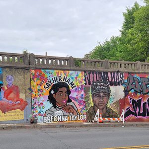 African-American woman with "Say Her Name Breonna Taylor" around her and graffiti writing on concrete wall