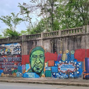 The words "I Can't Breathe" with painting of African-American man in green on concrete wall