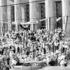 Crowd of people with signs on building steps with banner hanging above them