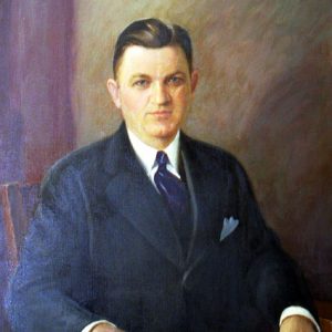 White man wearing a suit and tie sitting in a wooden chair