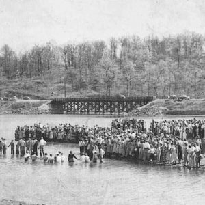 Crowd of people standing in or near a river with bridge in the background