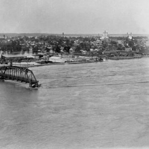 part of a bridge extending into a river with flooded city in background