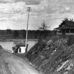 House with covered porch on hill next to steel truss bridge over river with small round building at its entrance