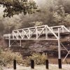 Steel truss foot bridge over creek with parking barriers in the foreground