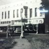 Multistory hotel and storefronts on street with signs street lamps and parked cars