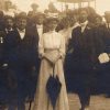 Crowd of white men and women in formal dress with horse drawn carriage behind them