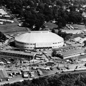 Oval-shaped stadium and surrounding buildings with residential area and trees in the background