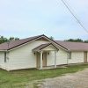 Single-story building with siding and covered porch on gravel parking lot