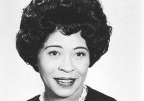 African-American woman wearing dark colored dress with double strain shell necklace