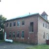 Side view of two-story brick school building with propane tank next to it and cupola on the roof