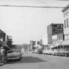 Multistory brick buildings on street with parked cars lined up in front of them and people on street corner