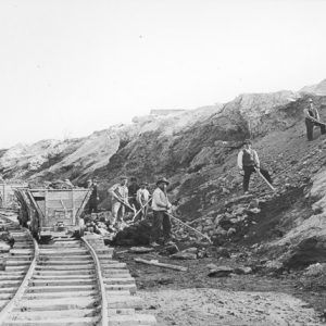 White miners filling small rail cars on a track with bauxite ore