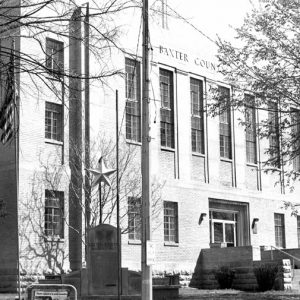 Three-story brick building with stone monument and trees