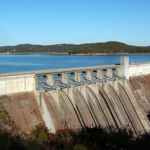 distant elevated view of dam holding back water and the dry spillway and embankment