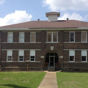 symmetrical two-story brick building with arched entrance and small tower