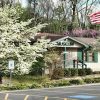 Single-story building with covered porch blooming trees and flag pole in front yard taken from parking lot