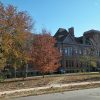 multistory brick building with tower and rows of windows and autumn trees in front