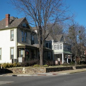 Row of multistory houses alongside street with short stone wall and trees in front