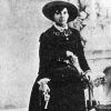 Old white woman in hat and dress holding a revolver