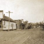 Dirt road with buildings on either side, including one "Dowell and Brown General Merchandise," and power lines