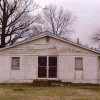 Front view of weathered cinderblock church building with double doors and cross on small steeple