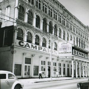 Multistory hotel building with arched windows with signs and covered walkway and columns on street