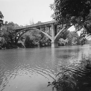 Side view of concrete arch bridge over river taken from shore