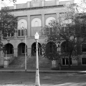 Multistory stone building with steep steps multi-arched entrance beneath classical facade and light posts in front