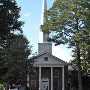 Brick church building with four columns and steeple with vehicle parked in front