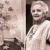 older white woman in cardigan and necklace poses while painting flowers