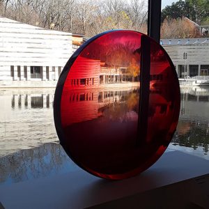 Modern buildings and pool seen through large red lens before window