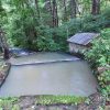 Looking down at multilevel spring with brick well building next to it in overgrown forested area