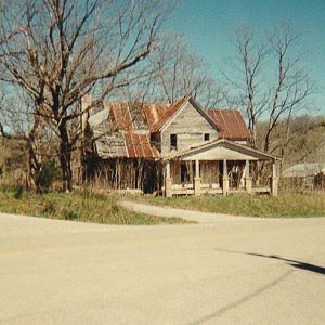 Abandoned multistory house with rusted metal roof on rural road