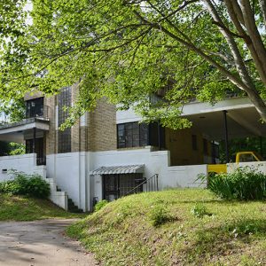 Multistory brick building with balconies and covered porch with tree in the foreground