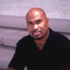 Bald African-American man with close-cropped beard and mustache sitting on steps in black shirt