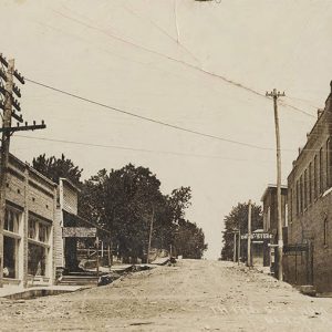 Multistory brick buildings on either side of dirt road with power lines crossing overhead