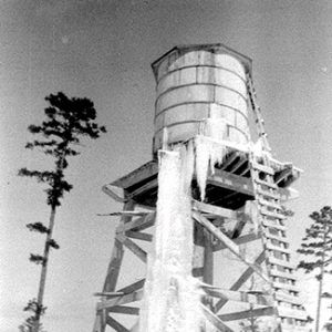 Ice on wooden water tower with truck parked nearby