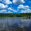 Lake with boats tied to shore with trees and mountains in the distance and blue skies