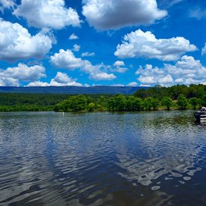 Lake with boats tied to shore with trees and mountains in the distance and blue skies