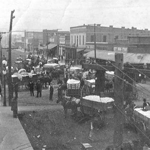 horse drawn wagons and pedestrians crowding busy street with brick buildings on either side