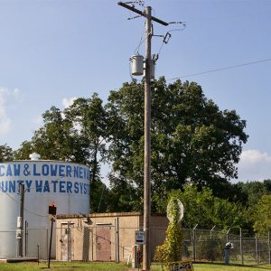 Round water tank and outbuilding inside fence with telephone pole standing outside it