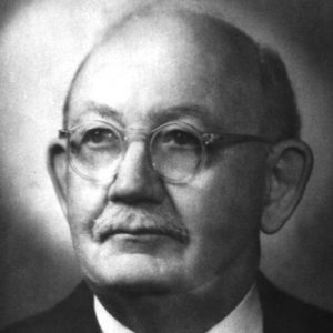 Portrait of balding white man with round glasses mustache wearing suit jacket and tie gazing contemplatively upwards