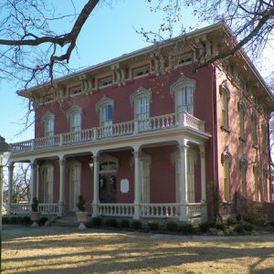 Two-story house with flat roof covered porch with balcony above it and gazebo behind house