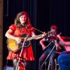 White woman in red dress playing acoustic guitar on stage