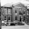 Multistory brick building with classical facade front steps large lawn bare trees and sidewalks