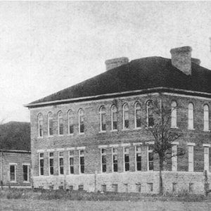 large two-story building with twin towers and arched windows and a smaller one-story building behind it