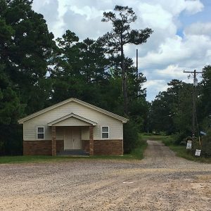 Single-story building with covered entrance on gravel road with power lines on its right side