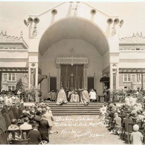 Crowd gathered outside at "Bishop's Jubilee" before exterior altar with stone building in the background